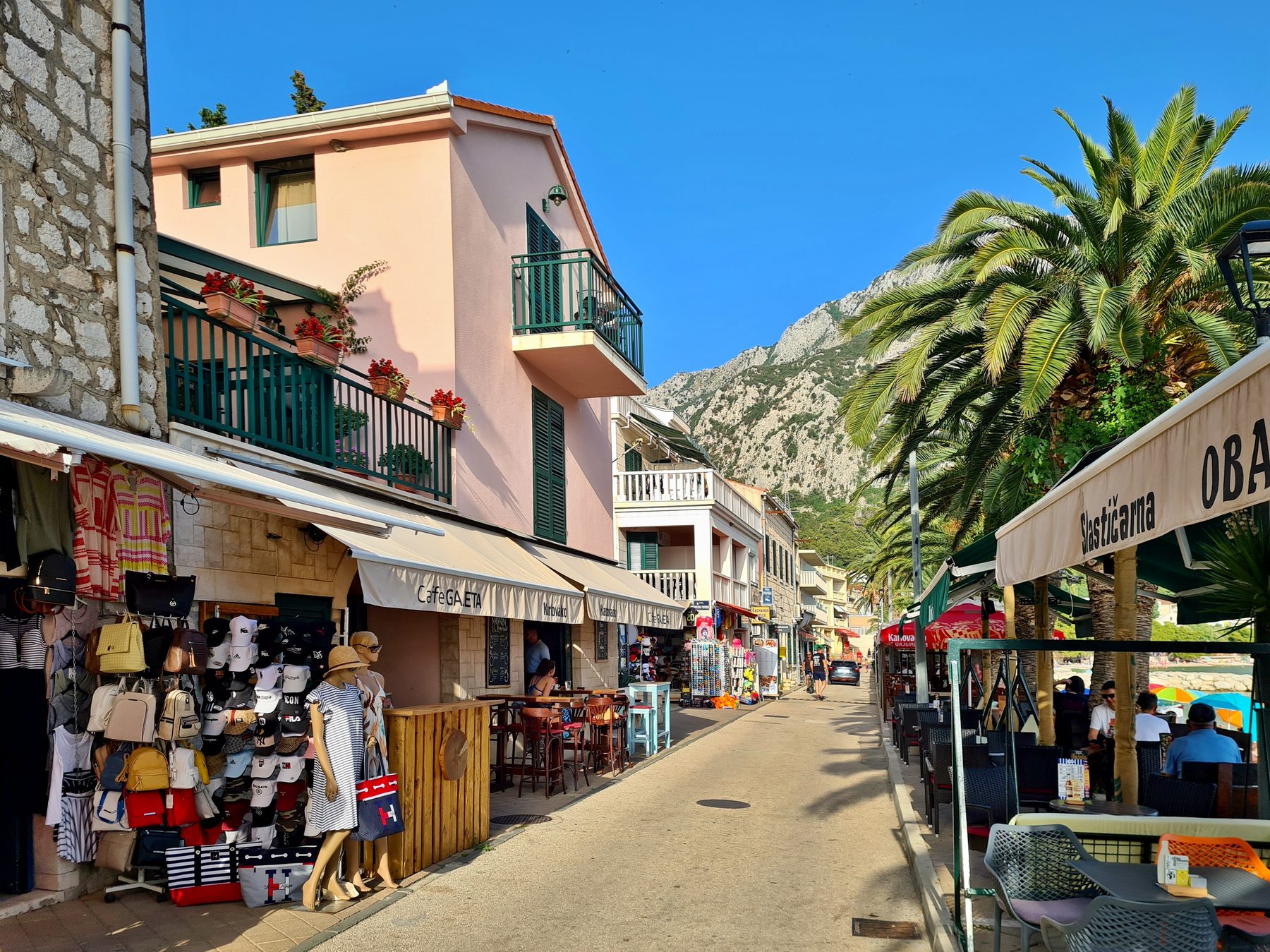 Street lined with small shops and outdoor cafes under palm trees in Gradac, Croatia