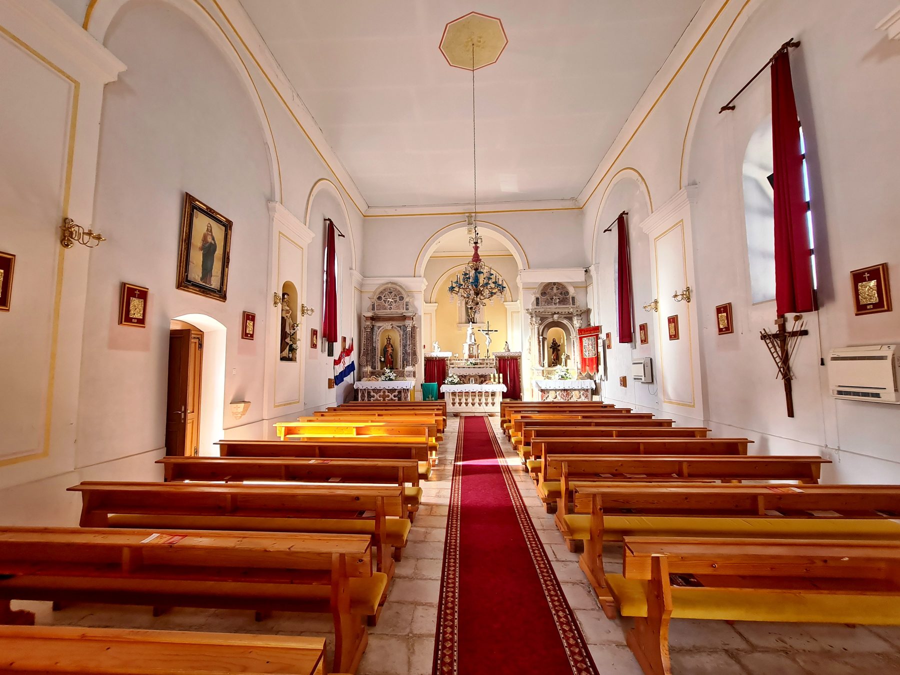 Interior of a church with wooden pews, red carpet aisle, and religious paintings in Općina Gradac, Croatia