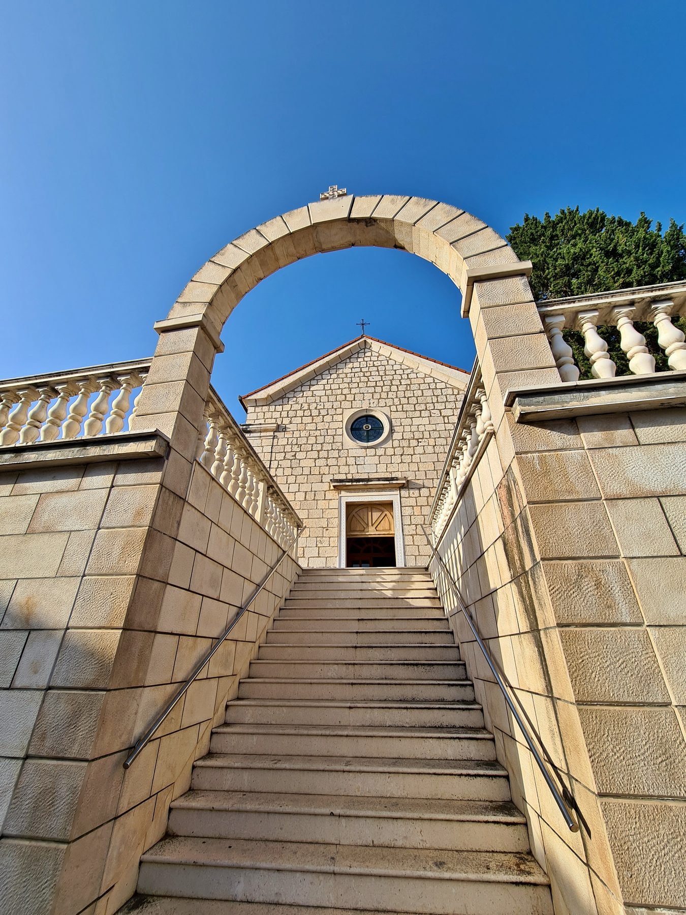 Stone staircase and arch leading to small stone church with circular window and cross