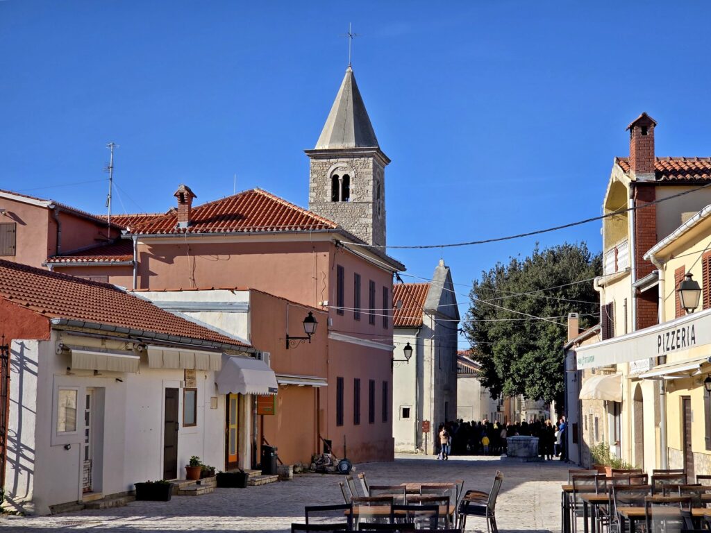 Historic church tower along a quiet street with outdoor seating and pastel buildings in Nin, Croatia
