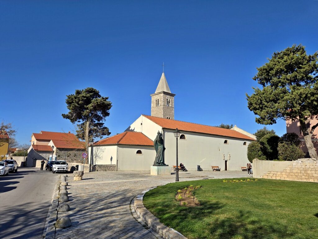 Church with a bell tower and statue in a sunny square in Nin, Croatia
