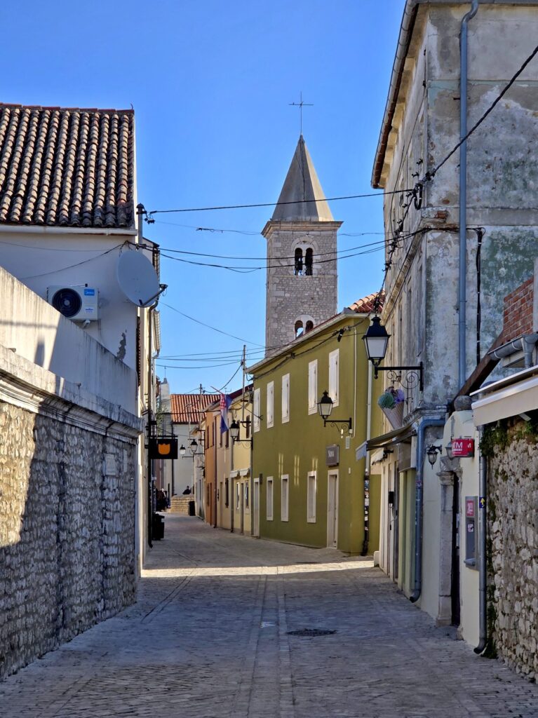Narrow cobblestone street and stone church tower in the old town of Nin, Croatia