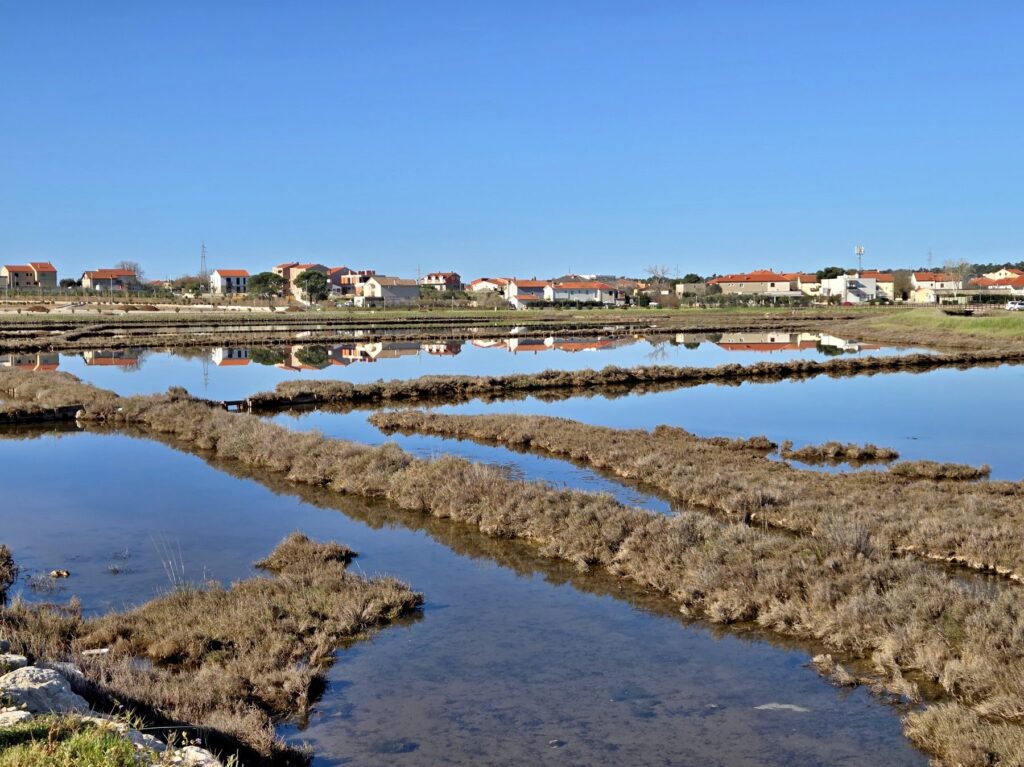 Salt flats with reflective water and houses in the village of Nin, Croatia under a clear blue sky