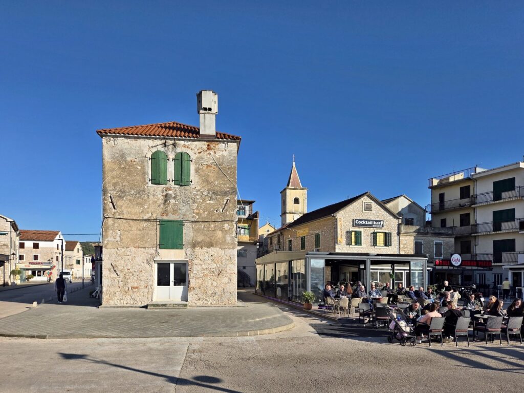 Outdoor terrace with people dining near old stone buildings in Pirovac, Croatia under clear blue sky