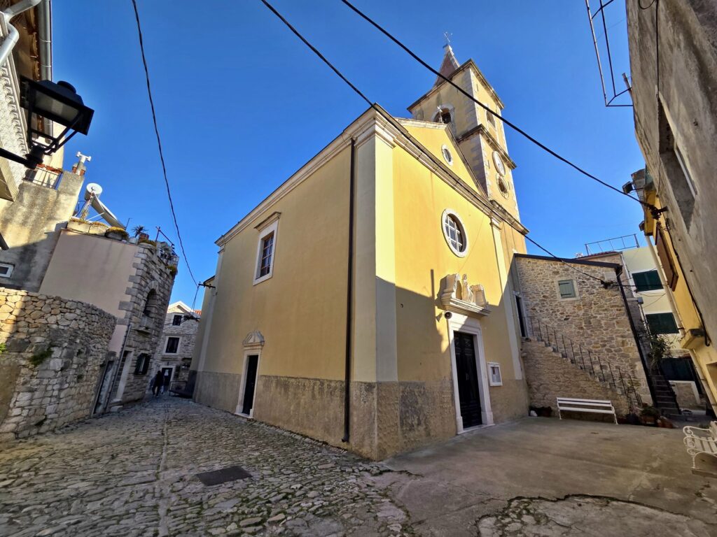 Historic church with yellow facade and clock tower in old town Pirovac Croatia
