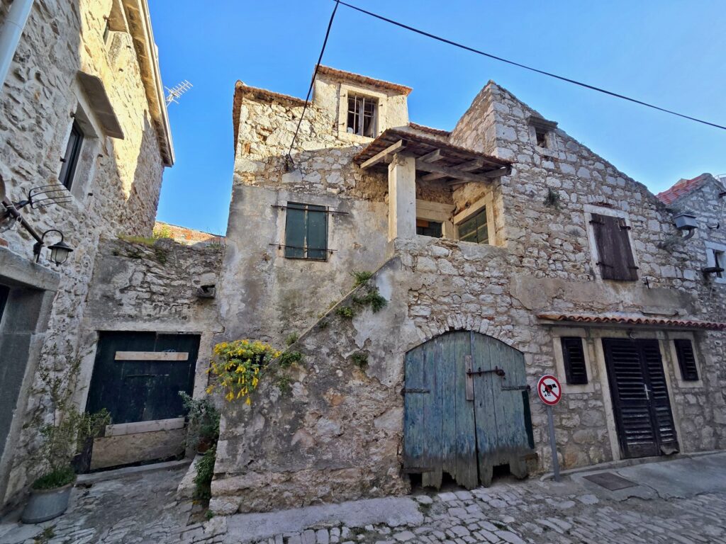 Old stone buildings with wooden doors and shutters in Pirovac, Croatia under clear blue sky