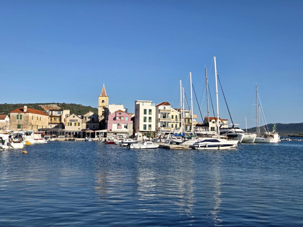 Pirovac harbor marina with sailboats and historic buildings under clear blue sky
