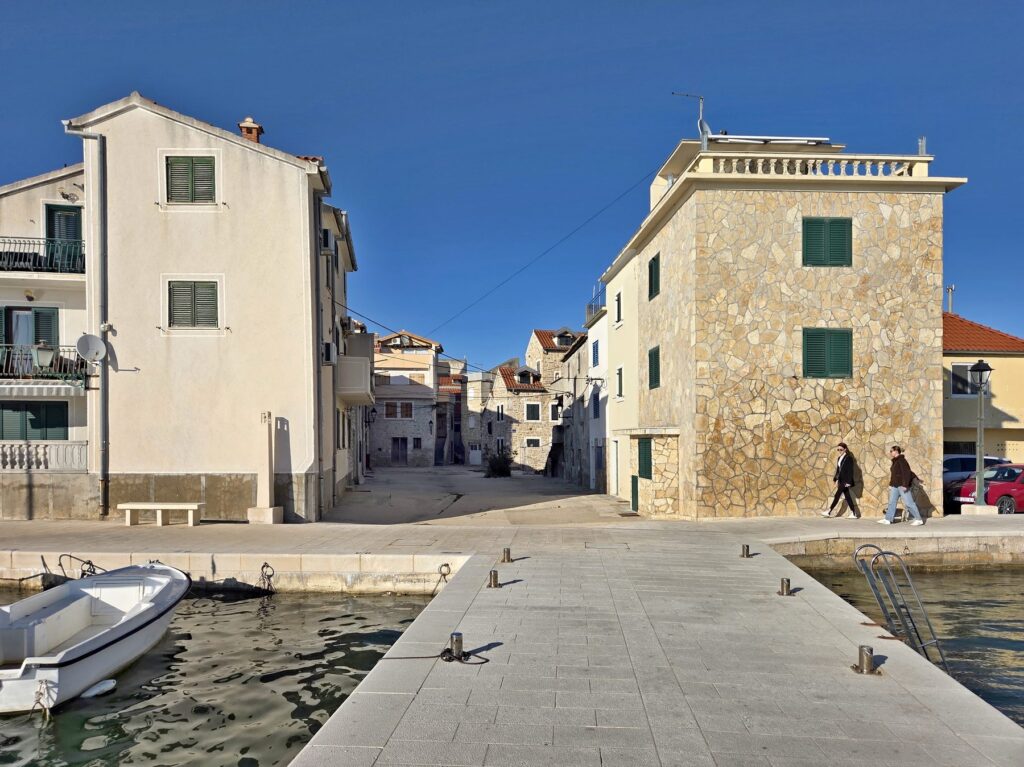 Waterfront promenade and small harbor in Pirovac, Croatia with stone buildings and clear sky