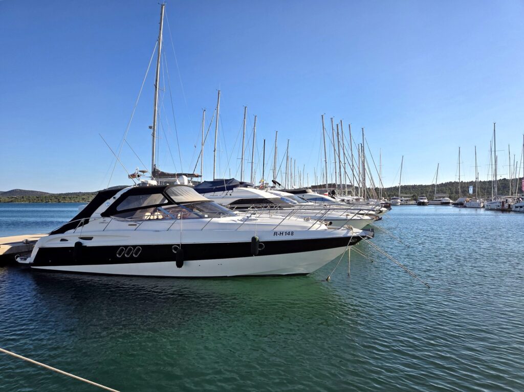 White motorboats and sailboats docked at a marina in Pirovac under clear blue sky