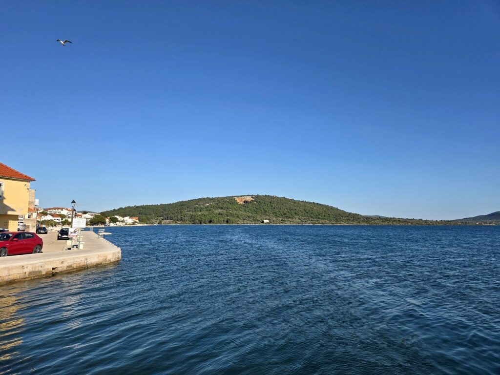Calm blue sea and green hill under clear sky at the Pirovac waterfront in Croatia