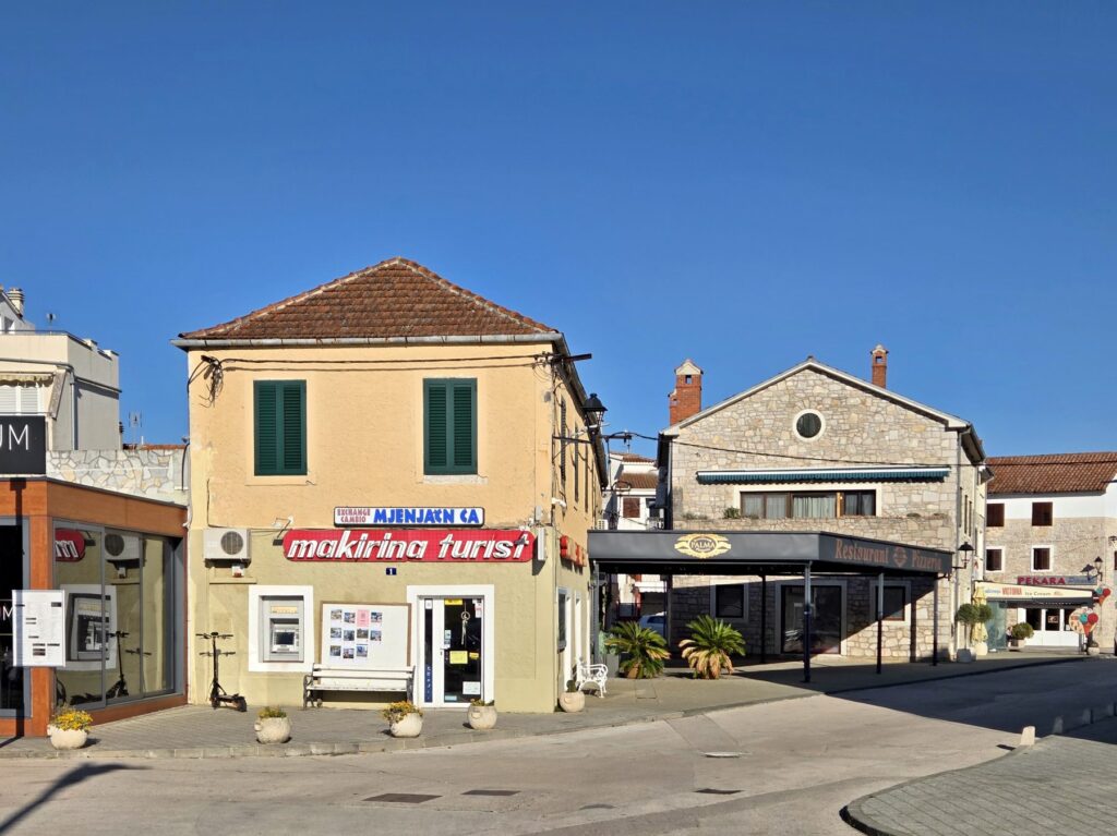 Sunlit street corner with a small tourist agency and a restaurant in Pirovac, Croatia