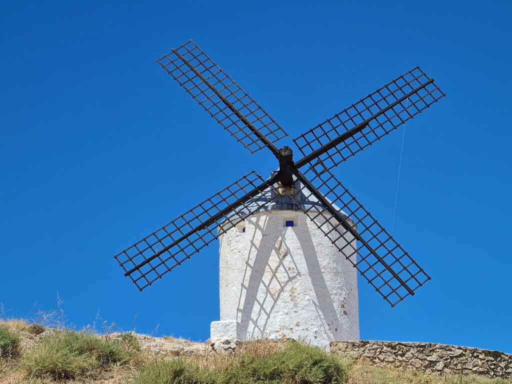 Traditional white windmill in Consuegra, Spain with large wooden sails and blue sky.