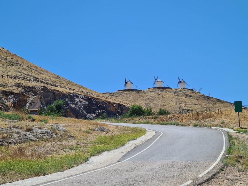 Curving road below the windmills of Consuegra, Spain on a dry hillside.